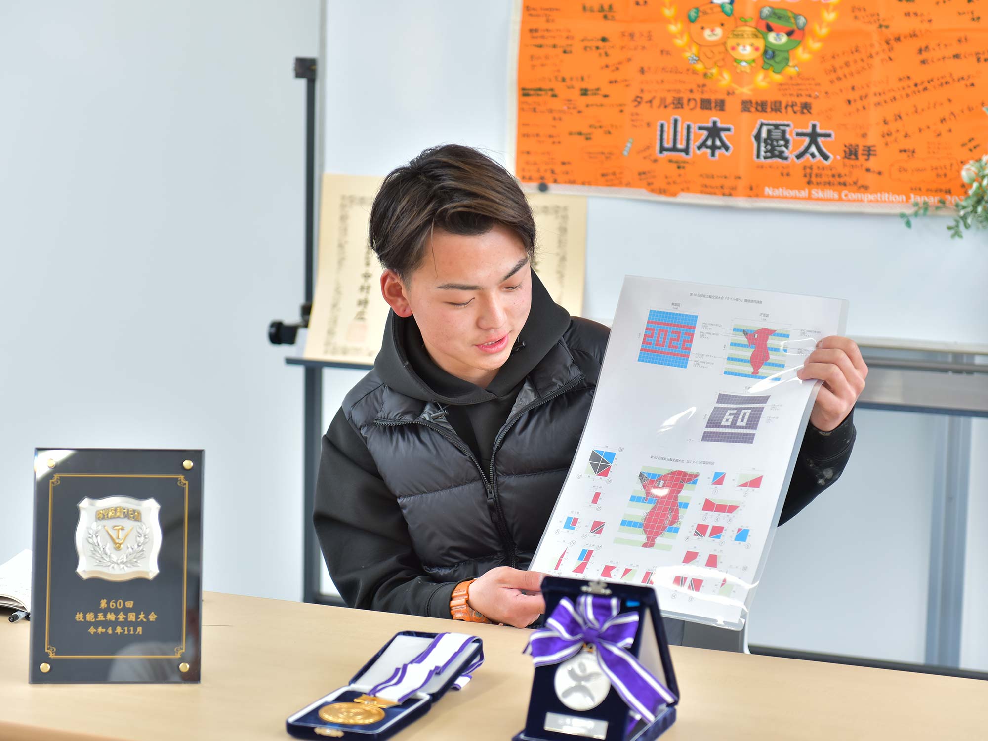 今大会の課題について話す山本さん。壁2面・床1面の合計3面を、墨出しから行い仕上げるものだという。